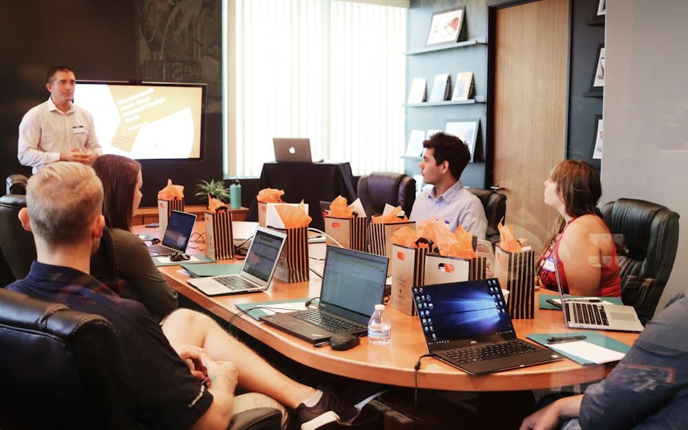 A facilitator presenting to a group seated around a table with laptops